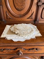 Various vintage linens stacked on a wooden antique dresser, showing intricate lace and crochet edges.