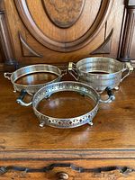 Three silver plate holders of varying sizes placed on a wooden surface with carved wood background.