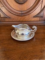Silver plated gravy boat with curved handle and matching underplate on wooden table