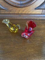 Two Venetian glass birds, one yellow and one red, placed on a wooden surface to show full profile and size