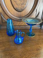 Three vintage cobalt blue glass items placed side by side on a wooden surface in front of a carved wooden background.
