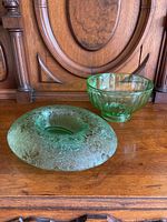 Two green vintage glass items on wood surface: a round punch bowl with vertical ribbing and a wide floral etched dish with frosted finish.
