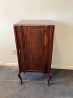 Front view of vintage wooden music sheet cabinet standing on carpet, showing rectangular door with brass handle.