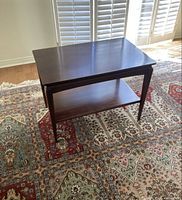 Side and angled view of the solid wood coffee table showing the rectangular top, lower shelf, and tapered legs on a patterned rug.
