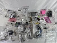 Overall view of small electronic components and mechanical parts in clear plastic bags spread across surface.