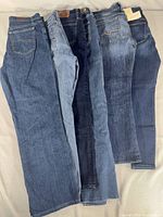 Six pairs of assorted women's blue jeans laid flat in a row to show various washes and styles.