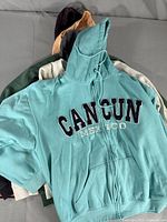 Teal Cancun Mexico zip-up hoodie on top of pile of assorted women's sweaters