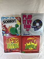 Four sealed board games: Sorry!, Play It By Ear 2, and two Apples to Apples Party Box editions.