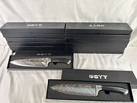 Photo of seven black GYY branded boxes stacked, with two open boxes displaying one brand new kitchen butcher knife each inside.