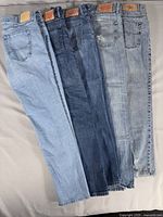 Five pairs of men's light wash denim jeans laid out side by side showing different shades and back pocket designs.