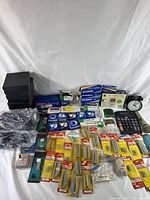 Photo of the entire lot showing stacked black boxes, numerous Sylvania projector lamp boxes, calculator, alarm clock, and various packaged small parts spread on a white background.