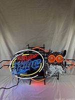 Full frontal view of neon sign showing Miller Lite logo with oval neon frame next to owl with bright neon eyes and orange detailing.