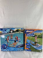 Photo showing two boxed items: a blue inflatable volleyball set by Bestway for ages 3+, includes net and ball, and a boxed Banzai Speed Blast Water Slide.