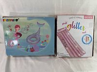 Two boxes side by side: one with the mermaid tail pool float by Sperpand featuring colorful underwater graphics, the other with an Intex pink glitter pool mat labeled 'Sand & Summer'