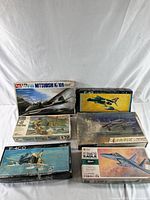 Full view of 6 vintage airplane model kit boxes stacked, various brands and styles visible, artwork showing different military aircraft models, some box wear.