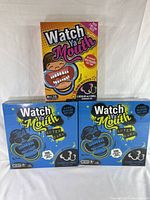 Front view of all three Watch Ya Mouth board games, one original edition and two After Dark editions in blue boxes.