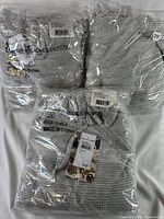 Three women's heather gray sweaters sealed in original packaging with price tags and Nordstrom Rack branding visible