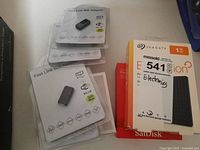 Five Fast Link USB WiFi adapters in sealed blister packs alongside SanDisk SSD and Seagate Expansion drive boxes