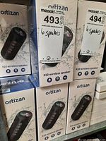 Six boxed Ortizan X10 wireless speakers stacked, showing front and side panels with branding and product info.