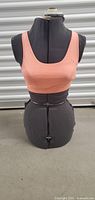 Front view of the vintage adjustable sewing mannequin bust covered in black fabric, showing peach sports bra for fit display.