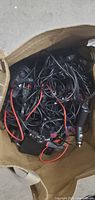 View of a paper bag containing tangled assorted wires including charging cables, car cigarette lighter power adapters, and connected rear view cameras.