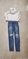 Photo of full outfit laid out, shows light grey American Eagle pullover hoodie and blue distressed skinny jeans with rips on knees