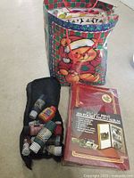 Photo of gently used paints in mesh holder, new photo album still in packaging, all inside a Christmas-themed gift bag with teddy bear design.
