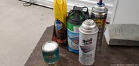 Lot of various paint cans and spray paint items displayed on a wooden table with a white storage background.