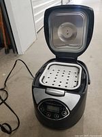 Front angled shot of the open black Burton portable cooker showing the interior perforated tray and power cord.