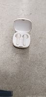 Overall photo of white wireless earphones inside the charging case with lid open, placed on a flat grey surface