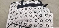Photo showing exterior of the tote bag with cream background and black geometric circle print. Two black handles visible at top along with a zipper.
