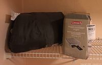 Black sleeping bag folded next to unopened boxed Coleman Raised Quickbed Queen air mattress.
