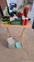 Photo showing the complete assortment of Avon collectibles on a wooden tray table, including several bottles, boxes, decorative containers, and the teal soap dish on its box.