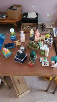 Wide view of Avon collectible perfume and cologne bottles arranged on a wooden table with some cardboard boxes in background.