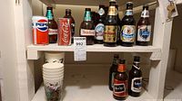 Full and empty collector beer and pop bottles displayed on shelves, including Pepsi can, Coca-Cola bottle, various Heidelberger bottles.