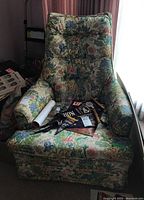 Front-facing view of floral fabric occasional chair showing full upholstery, armrests, and removable zippered seat cushion with some items placed on it.