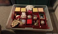 Plastic tote container with multiple boxed and loose vintage Christmas ornaments inside, some unpacked and some still in yellow packaging.