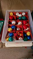 Photo showing plastic tote with assorted colorful spherical Christmas ornament balls separated by red cardboard dividers.