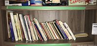 Wide view of assorted cookbooks placed on a bookshelf with various titles visible, showing age and use wear.