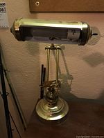 Front angle view showing the cylindrical lamp shade, switch, and the brass base with adjustable arm.