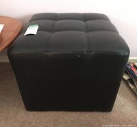 Black leather footstool showing front and top tufted stitched pattern.