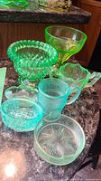 Photo showing multiple uranium and depression glass pieces including bowls and creamer on a countertop
