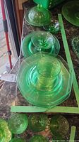 Various green glass pieces aligned on the counter, including plates, candle holders, butter dish with lid, and a glass.