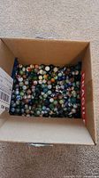 Cardboard box filled with numerous glass marbles