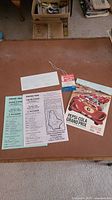 Photo showing full set of items flat on surface: official race program with illustrated racing cars cover, a green admission ticket, event outline sheet, circuit map, and ticket tag.