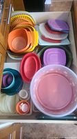 Top-down view into drawer with assorted plastic bowls, colanders, small containers and lids in various colors including pink, purple, orange, yellow, green.
