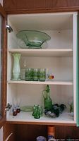 Full view inside cabinet showing multiple shelves with vintage green glass pieces including bowl, vase, glasses, decanter, and decorative items.