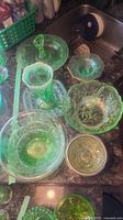 Photo showing multiple pieces of vintage green glassware including a three-tiered serving tray, bowls, and a vase, highlighting the intricate patterns and light green color.