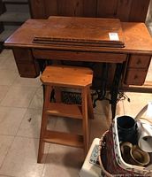 Vintage oak Singer sewing machine stand with cast iron treadle base, drawers on each side, and hinged top cover closed over sewing machine surface. Accompanied by a wooden stool.