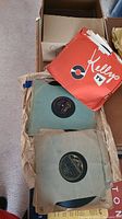 Open box revealing several 78 RPM vinyl records in red Kelly's sleeves and plain paper sleeves.